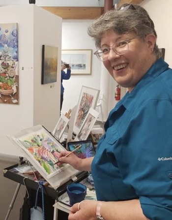 A woman is smiling at the camera, showcasing a joyful expression. The setting appears to be indoors with a wall in the background. She is likely enjoying the moment, possibly surrounded by art or books in her room.