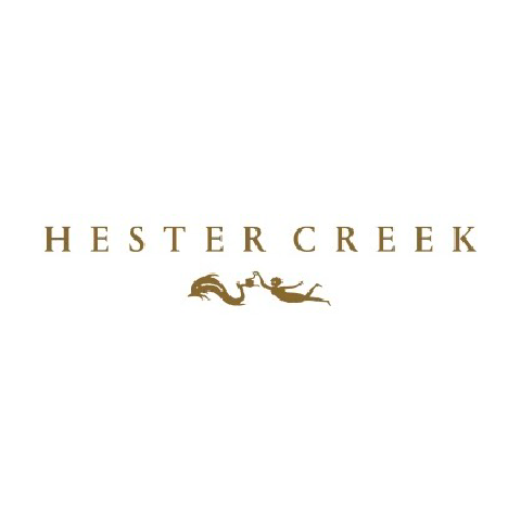 The image is a logo against a white background. At the top center of the image, the words "HESTER CREEK" are displayed in all capital letters. The font is a classic serif style, and the color of the text is a deep, warm golden brown. Below the text, there is a silhouette of a stylized mythological creature, resembling a dragon or a sea serpent, interacting with a human figure. The creature is on the left, depicted with flowing lines suggesting movement, and it appears to be either reaching for or being offe