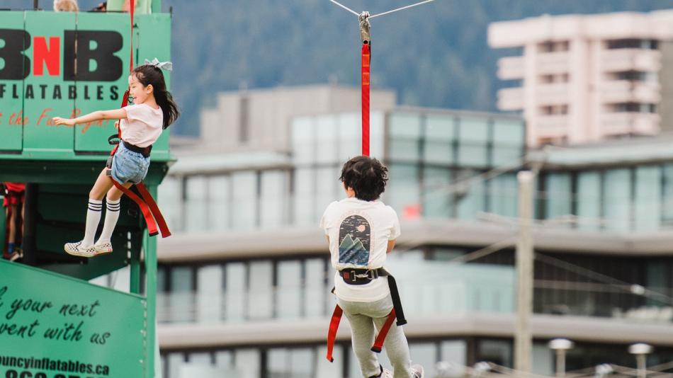 Two children on a rope swing in front of a building, enjoying a zipline ride together.