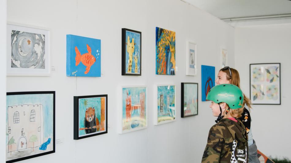 A boy and a girl observe artwork displayed in a gallery, engaged in thoughtful discussion about the pieces.