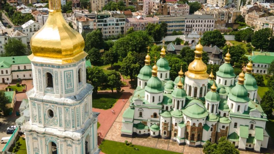 The image is of a large building with a gold-domed roof surrounded by trees. It is a cathedral in Ukraine known as St. Sophia's Cathedral in Kiev, as seen from the height of St. Sophia's Square in the cityscape.