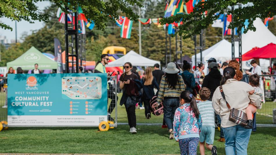  People stroll through a festival entrance adorned with a sign reading "West Vancouver Community Cultural Fest" during a vibrant day.