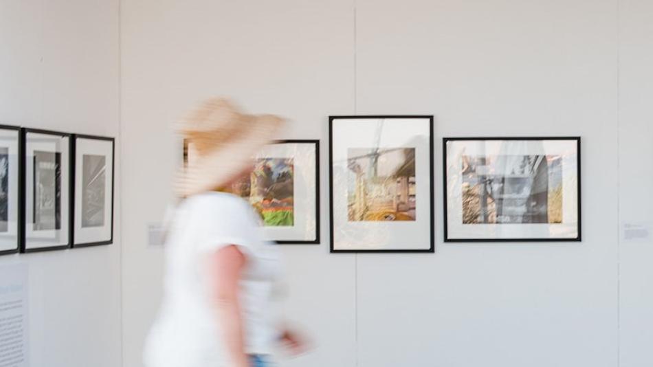 A woman strolls through an art gallery, admiring framed photographs displayed on the walls.