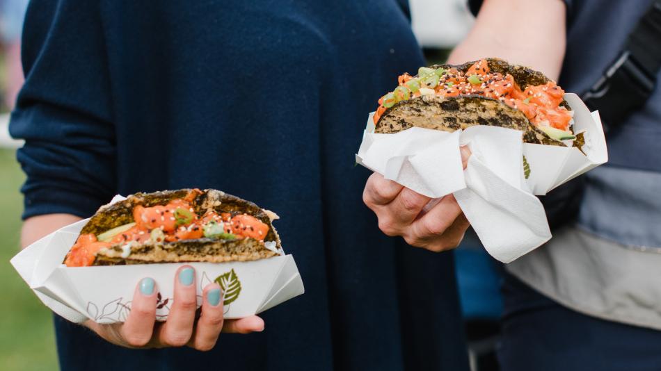 Two hands holding tacos made with nori and filled with salmon.