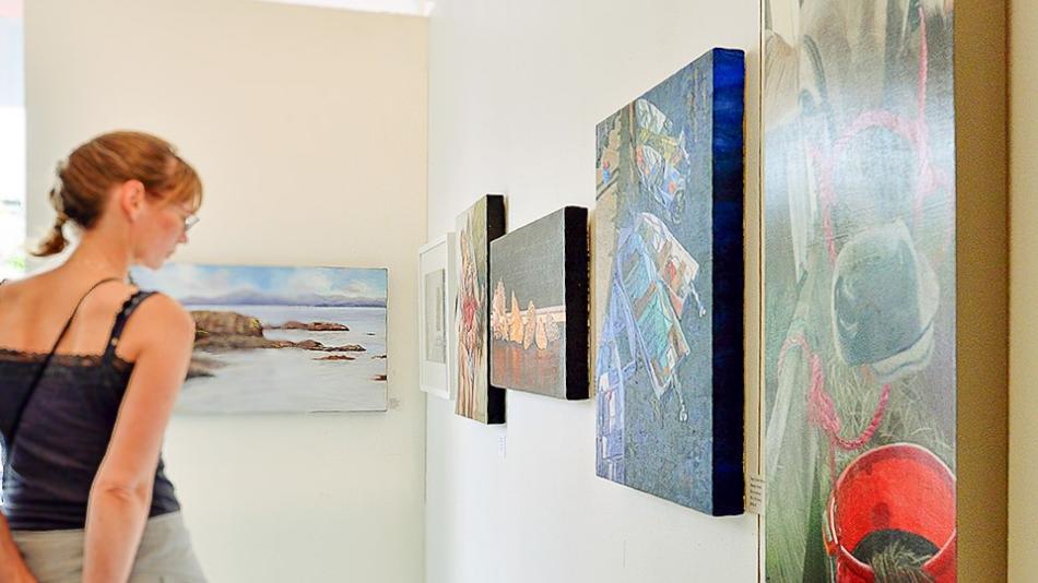 A woman examines a collection of paintings hanging on a wall in an art gallery.