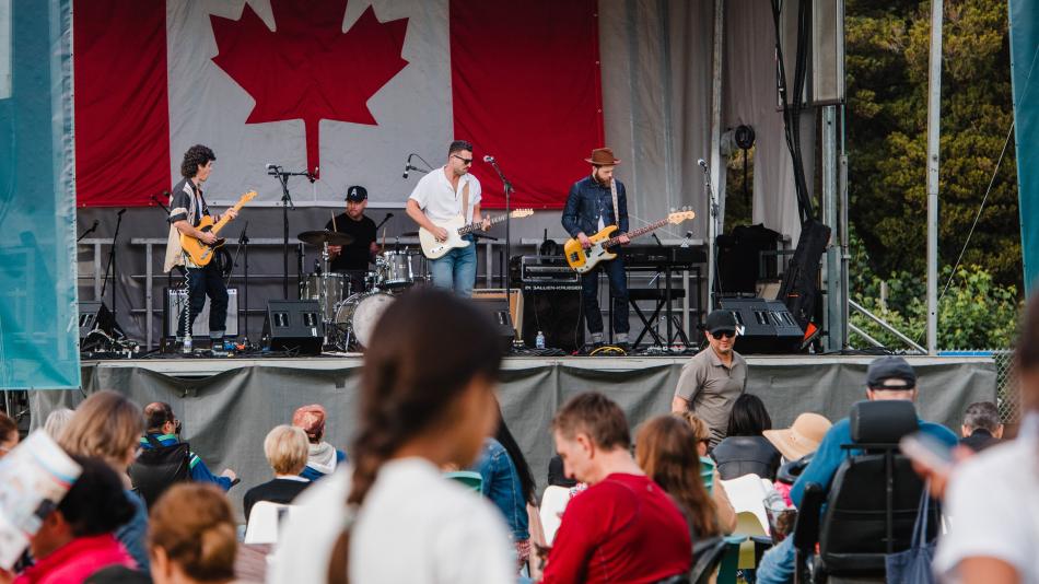 A band performs energetically on stage, with a prominent Canadian flag displayed in the background.