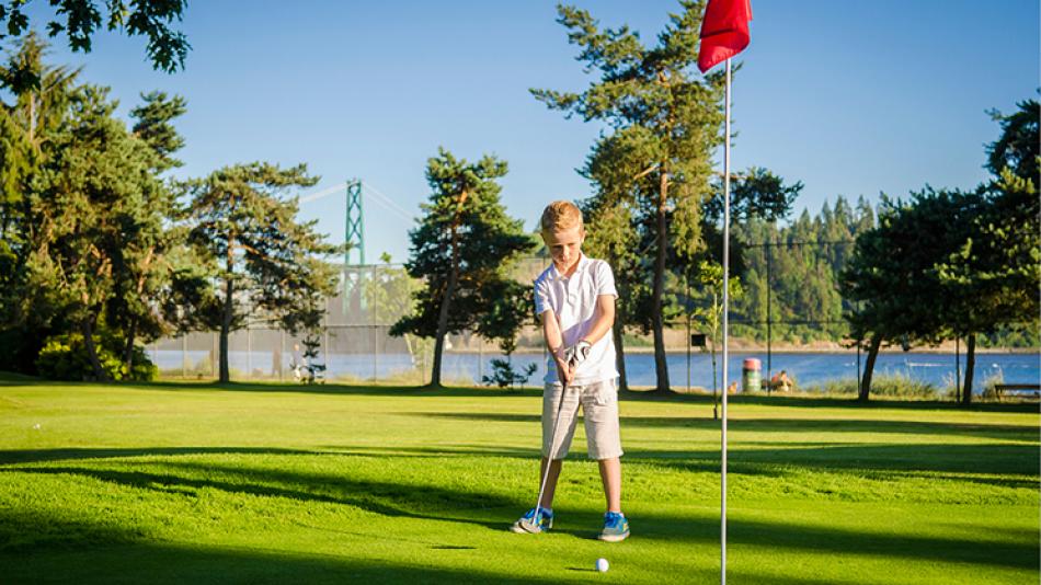 A child putts a golf ball toward the hole marked with a red flag.