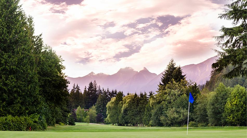 A hole at Gleneagles Golf Course with a blue flag marker and mountains seen past the trees in the distant.