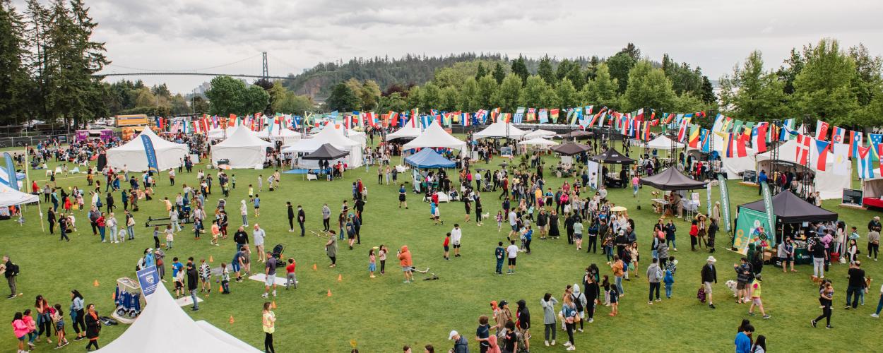 Large field with many tents and flags, with lots of people walking around 