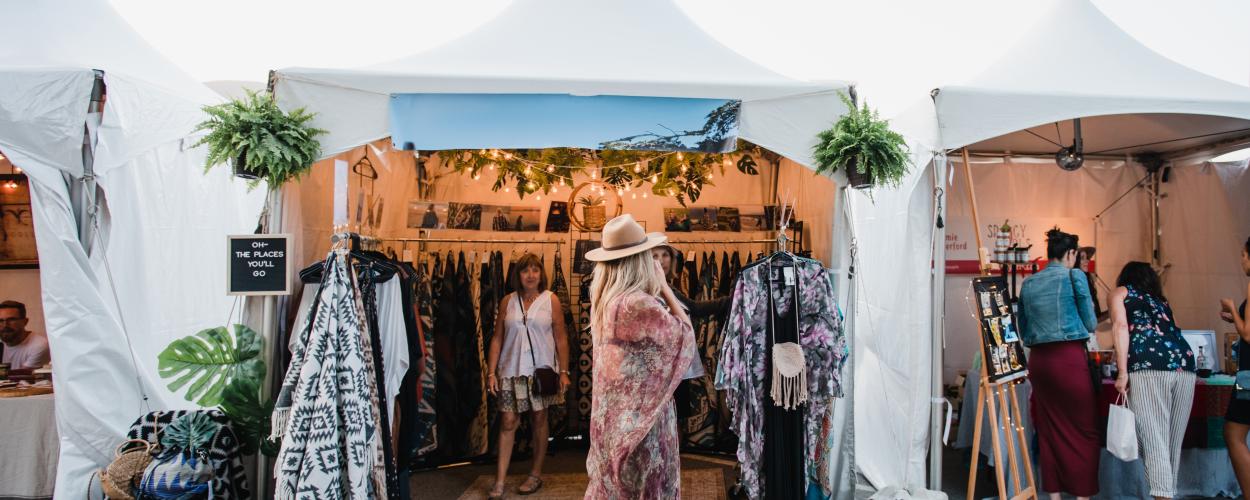 A woman strolls through a vibrant art market, exploring various tents filled with unique items.
