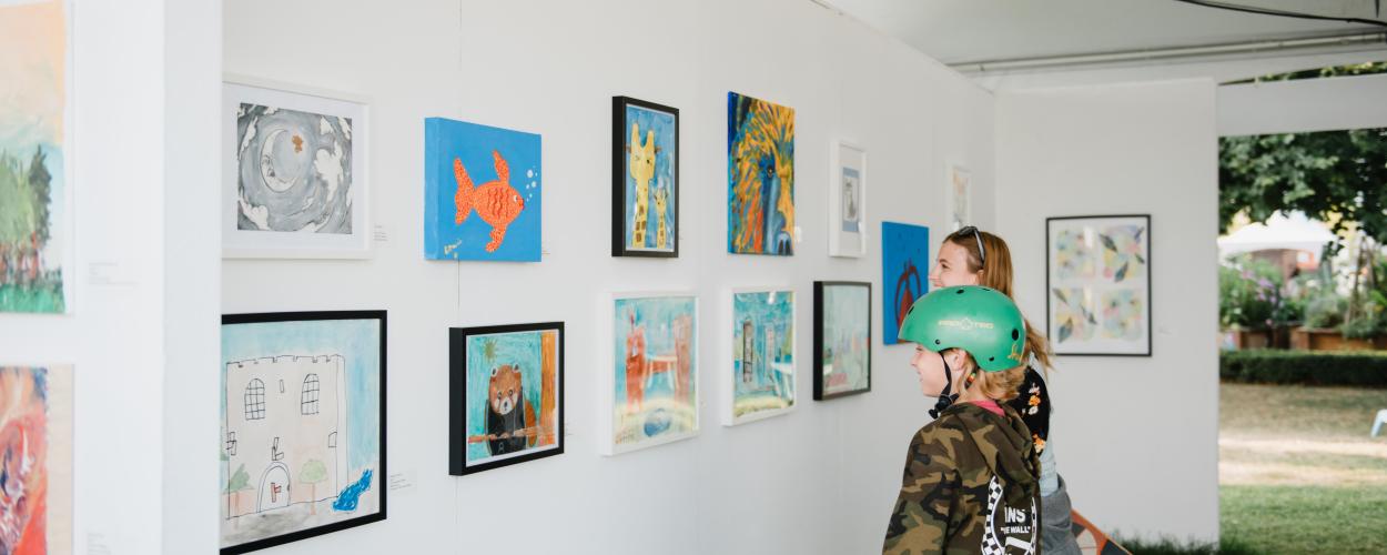 A boy and a girl observe artwork displayed in a gallery, engaged in thoughtful discussion about the pieces.