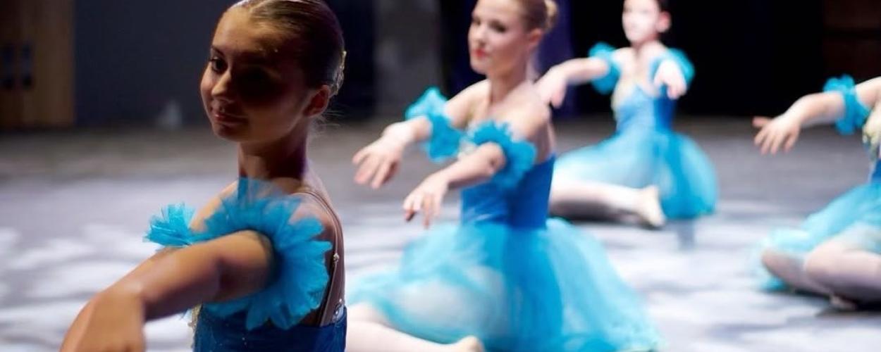 A group of young ballerinas in blue dresses performing ballet together in a studio setting.
