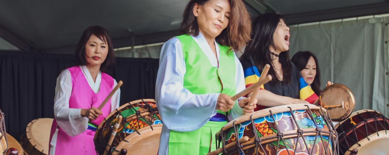 A group of women playing traditional Korean drums at a vibrant festival, showcasing their cultural performance and unity.