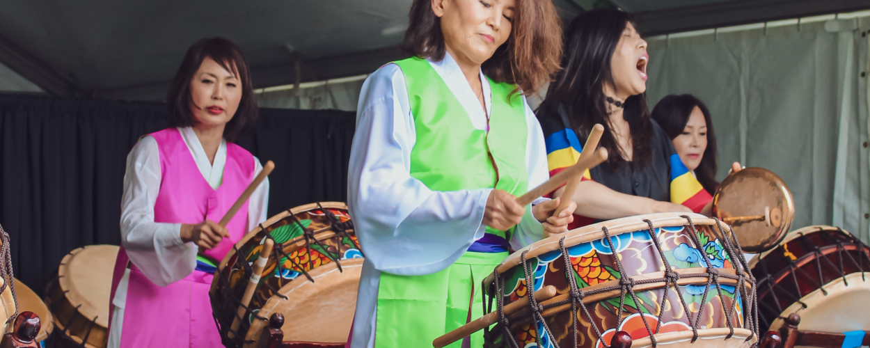 A group of women dressed in traditional attire joyfully playing drums together in a vibrant cultural celebration.