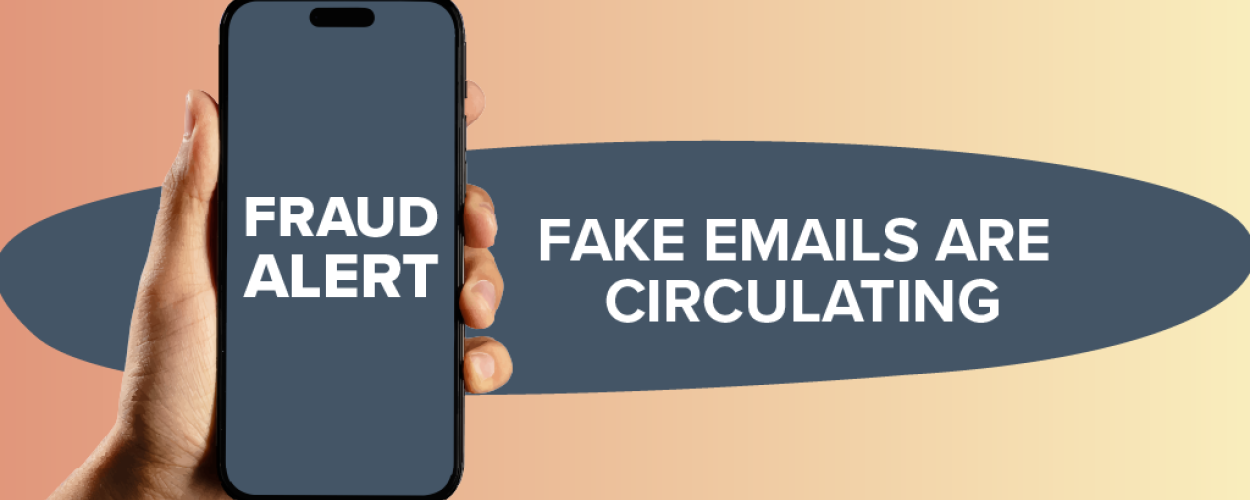 The image displays a modern, graphic presentation of a fraud alert. A hand is holding a dark-colored smartphone in the foreground, positioned slightly to the left of center. The phone's screen is illuminated and shows bold, white text that reads "FRAUD ALERT" stacked in two lines. The phone itself has a sleek, contemporary design with a black bezel and a notch at the top.
