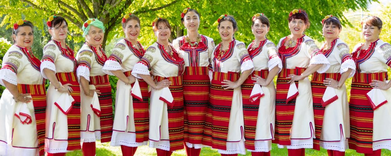 A group of women from Kitka, Hubavitz, and Duo Balkanaria posing together in colorful traditional costumes for a photo.