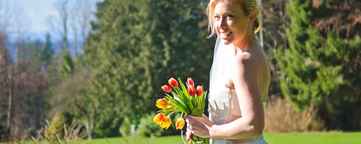 A bride stands in front of a forested area holding a bouquet of tulips.