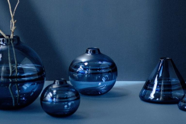 The image features a collection of blue glass objects, showcasing their vibrant cobalt hue. These pieces are arranged in a still life composition, emphasizing their transparency and reflective qualities. The setting is indoors, allowing for rich lighting that enhances the beauty of the glass. The overall aesthetic captures the elegance and artistry of these decorative vases.