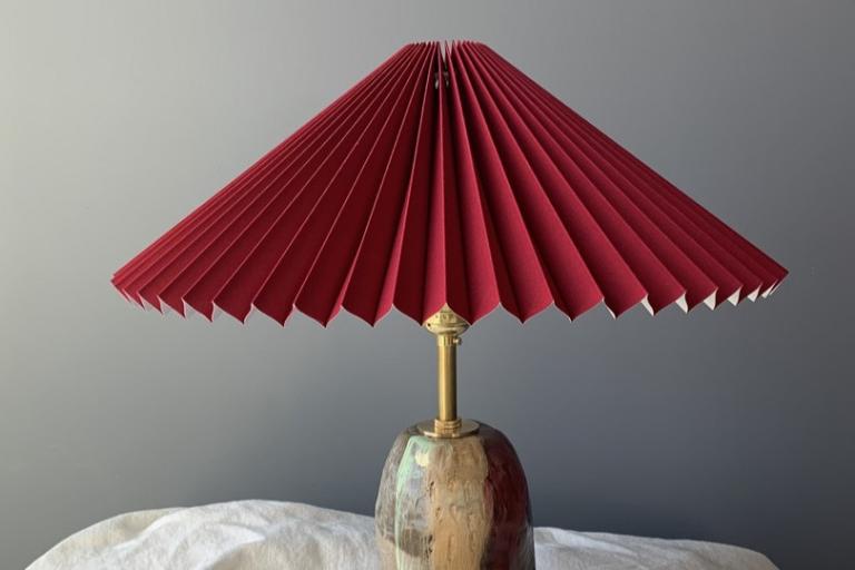 The image is a close-up, still life photograph of a decorative table lamp. The lamp is positioned in the lower center of the frame, angled slightly towards the viewer.