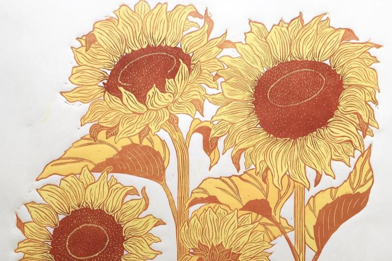 The image is a linocut print of sunflowers on a white background. The print is rendered in two colors: a warm, deep reddish-brown and a bright, sunny yellow. The sunflowers are depicted in various stages of bloom, with three prominent, large blooms and at least one smaller, partially visible bloom.
