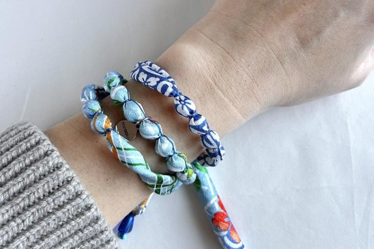 The image displays a close-up shot of a person's wrist and arm adorned with multiple fabric bracelets. The bracelets are the primary focus, and they are constructed from fabric that has been tied around small, bead-like forms. These forms create a textured, segmented appearance for each bracelet.