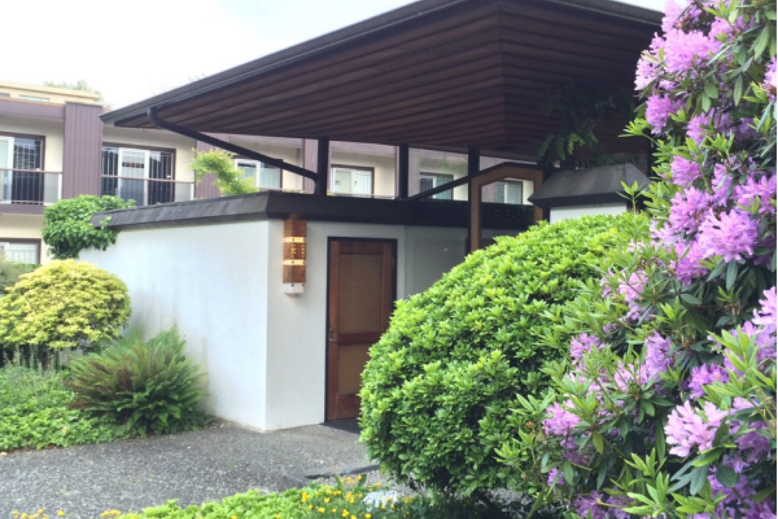 A corner of the exterior of the Woyat-Bowie building, including a tall shrub with purple flowers near the enterance.