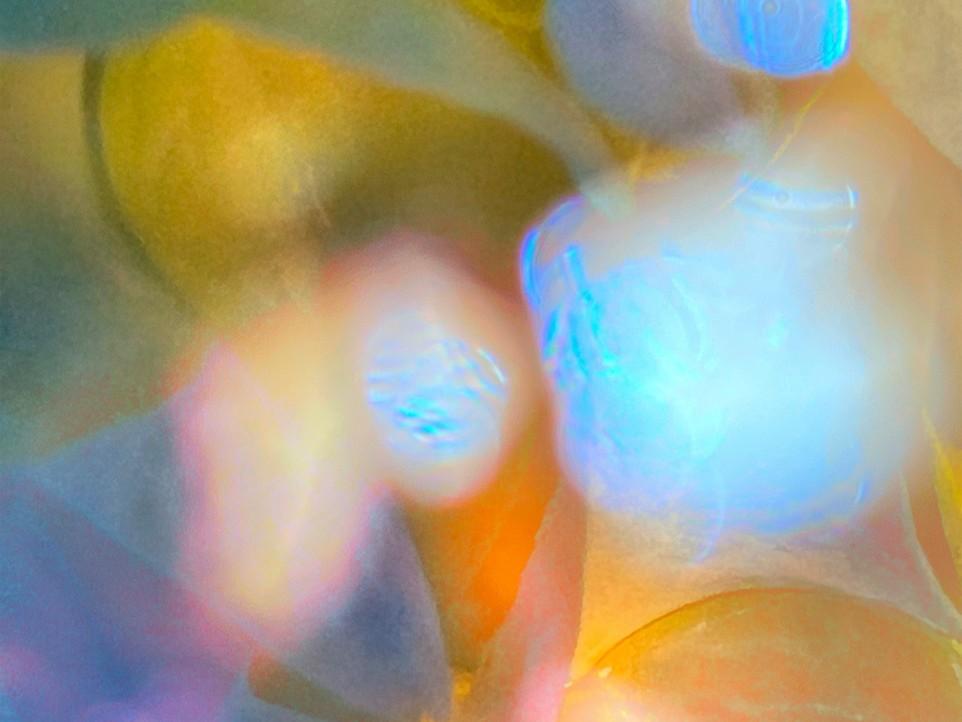 This is an abstract, blurry, and brightly colored image that appears to be a macro shot of some sort of reflective or translucent material, possibly illuminated by colored lights.