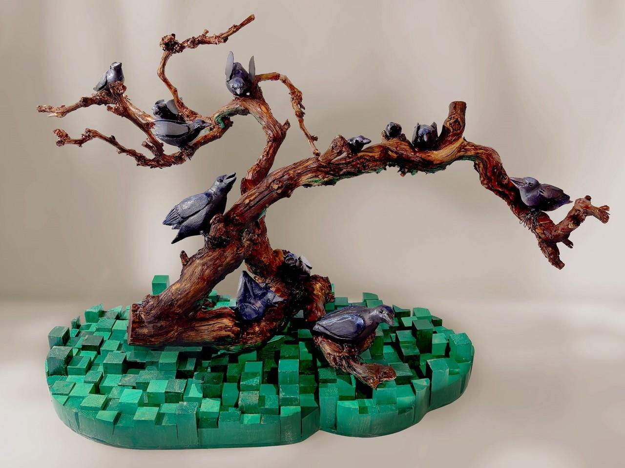 This is a photograph of a sculpture depicting a gnarled tree branch with several birds perched on it, resting on a green, pixelated base.