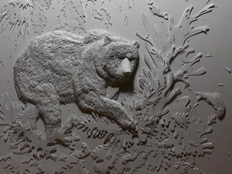 This is a detailed bas-relief sculpture made of a light gray material, possibly plaster or a similar medium. The artwork depicts a grizzly bear in a dynamic scene of fishing.