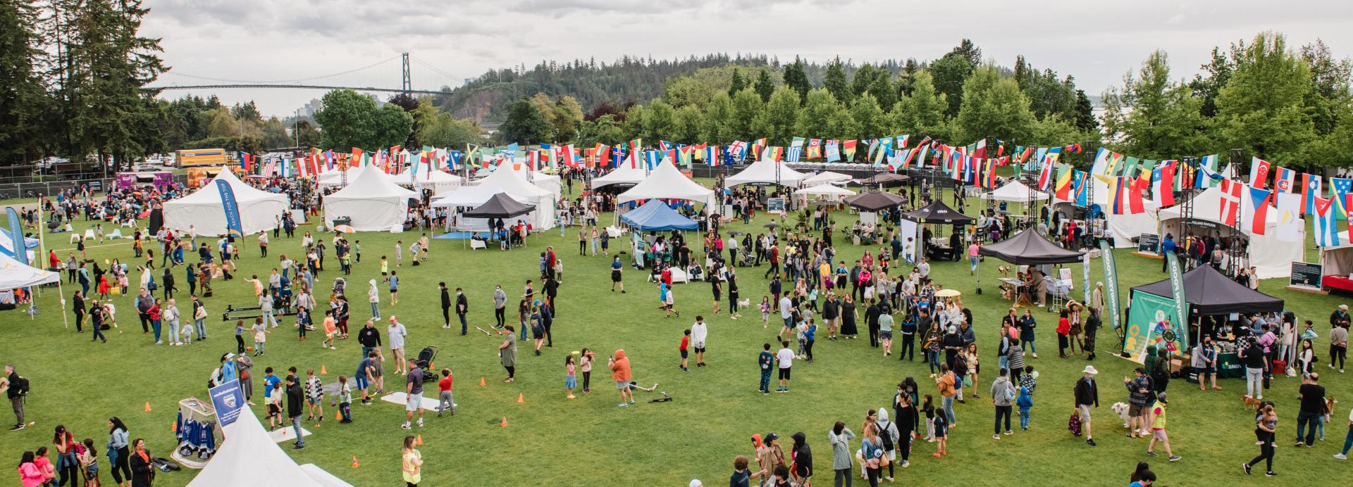 Large field with many tents and flags, with lots of people walking around 