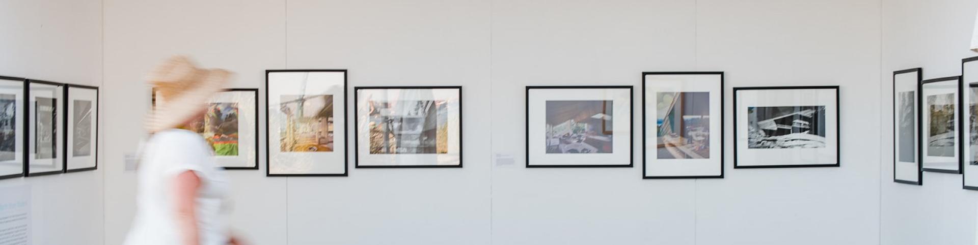 A woman strolls through an art gallery, admiring framed photographs displayed on the walls.