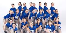 A group of young girls in blue uniforms, dancing while wearing American football shirts, showcasing their energetic performance.