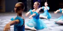 A group of young ballerinas in blue dresses performing ballet together in a studio setting.