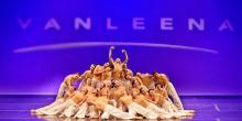 Full shot of a large group of dancers, likely a dance troupe, performing a contemporary dance.   The dancers are arranged in a complex, layered formation, with some dancers positioned atop others, forming a sort of pyramid or stacked arrangement. 
